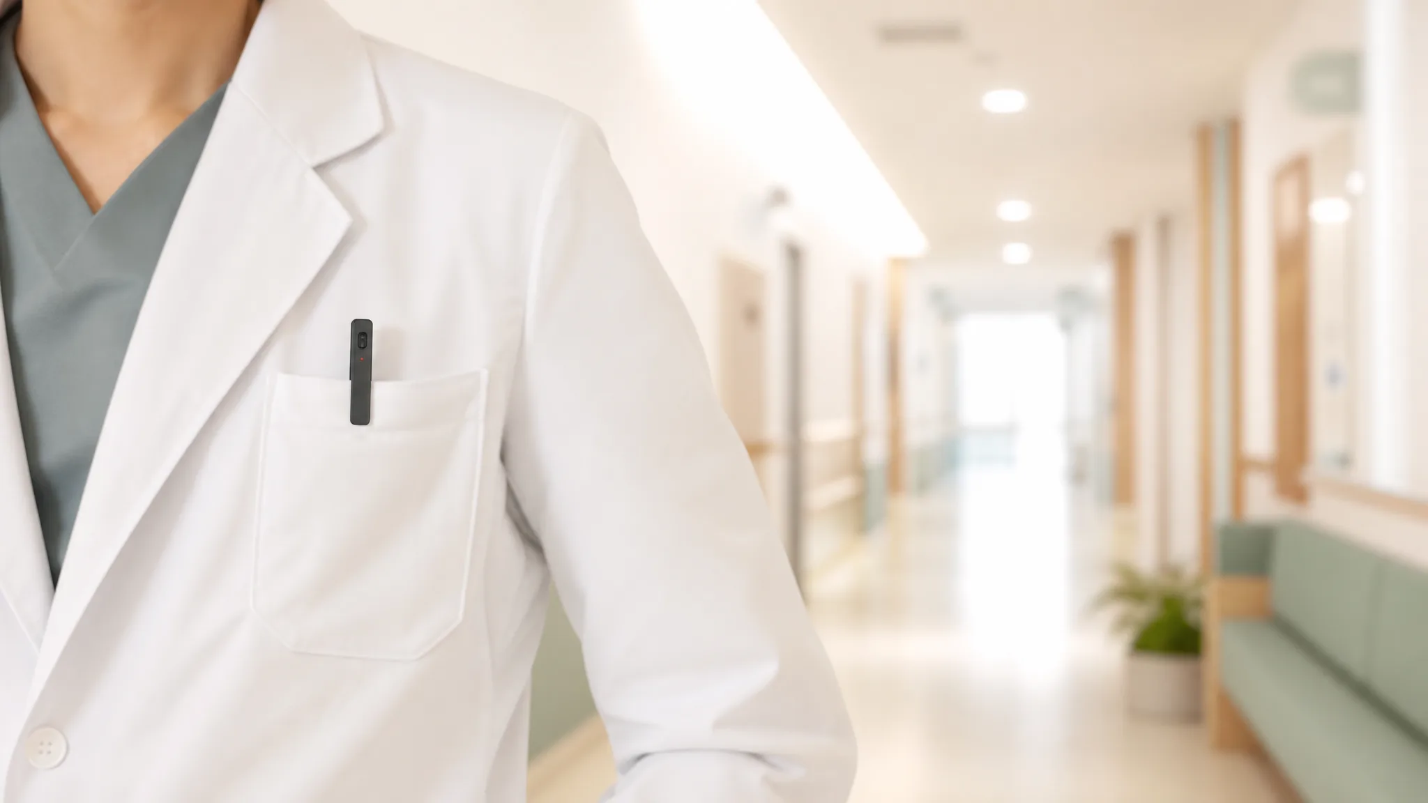 A white coat with a slim recorder peeking from the chest pocket, hospital corridor bokeh